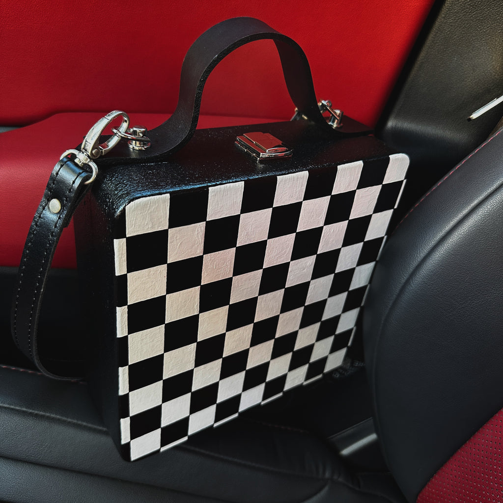 Black and white checkered wooden handbag with leather strap on car seat, handmade artistic accessory.
