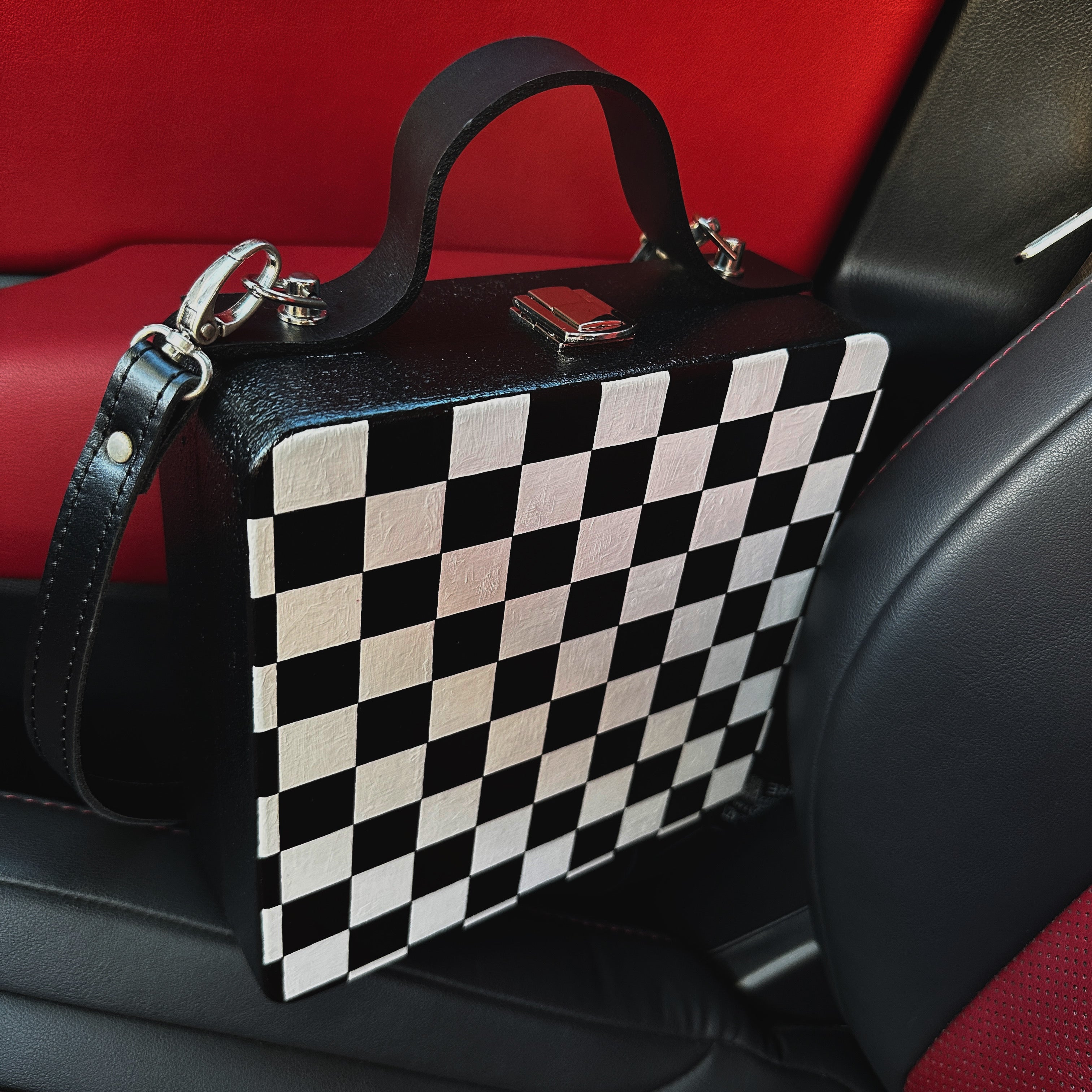 Black and white checkered wooden handbag with leather strap on car seat, handmade artistic accessory.