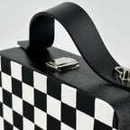 Black and white checkered wooden handbag with leather strap on car seat, handmade artistic accessory.