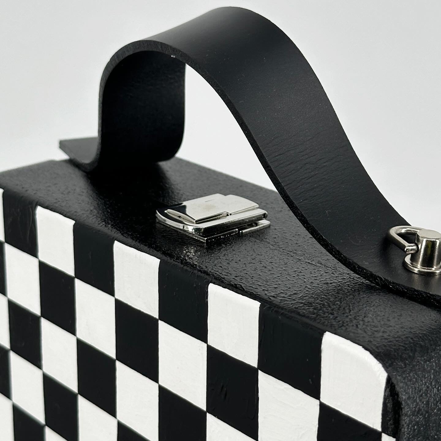 Black and white checkered wooden handbag with leather strap on car seat, handmade artistic accessory.