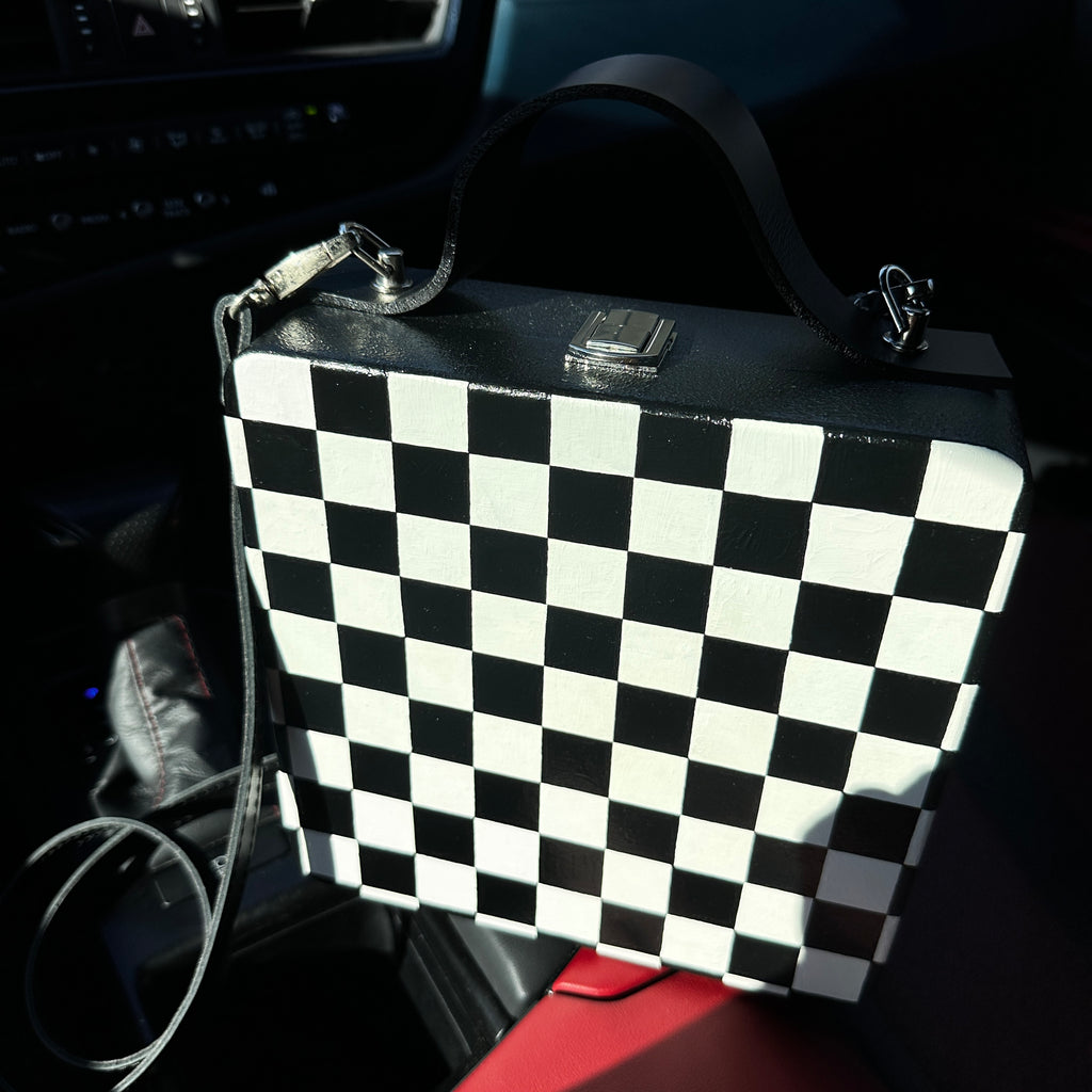 Black and white checkered wooden handbag with leather strap on car seat, handmade artistic accessory.