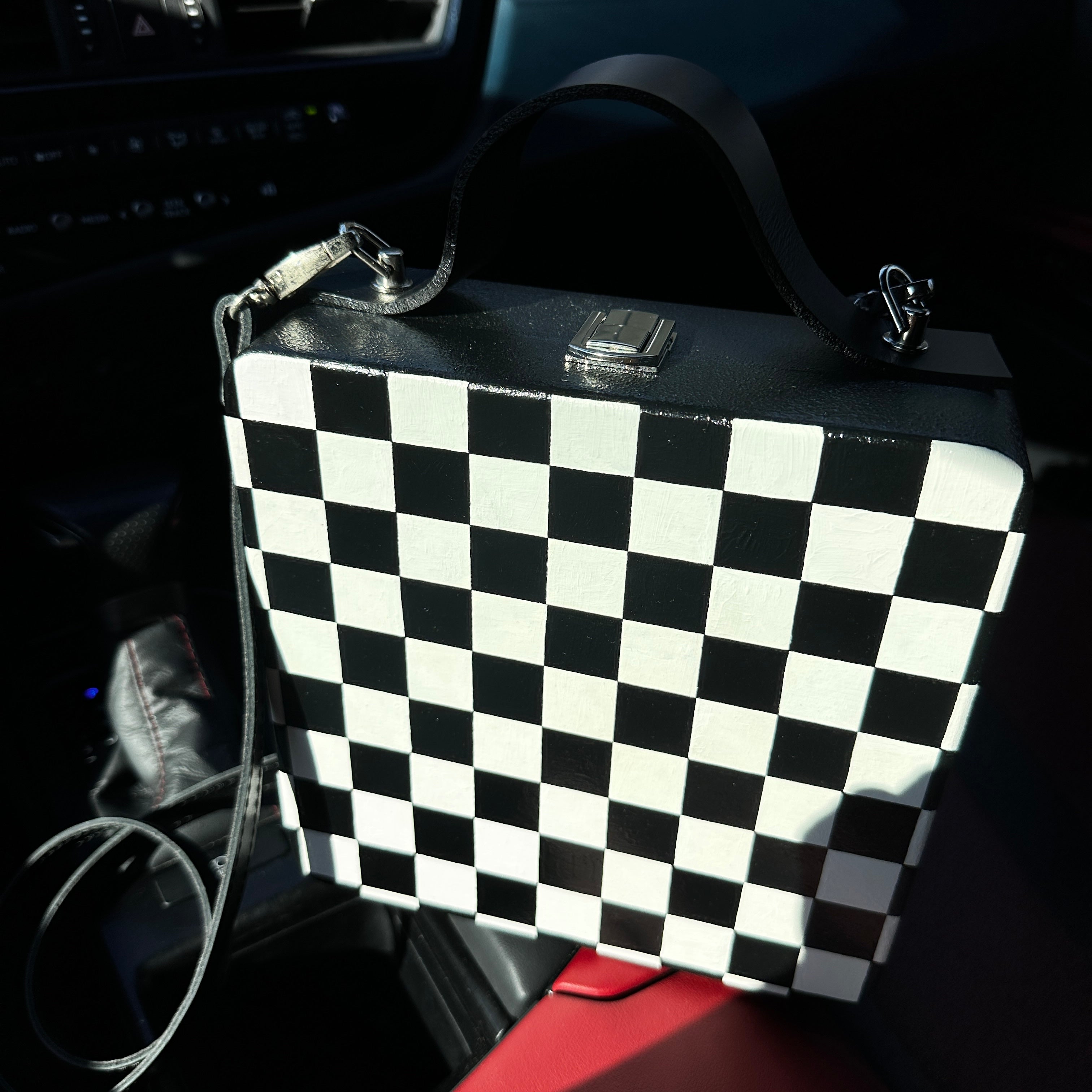 Black and white checkered wooden handbag with leather strap on car seat, handmade artistic accessory.