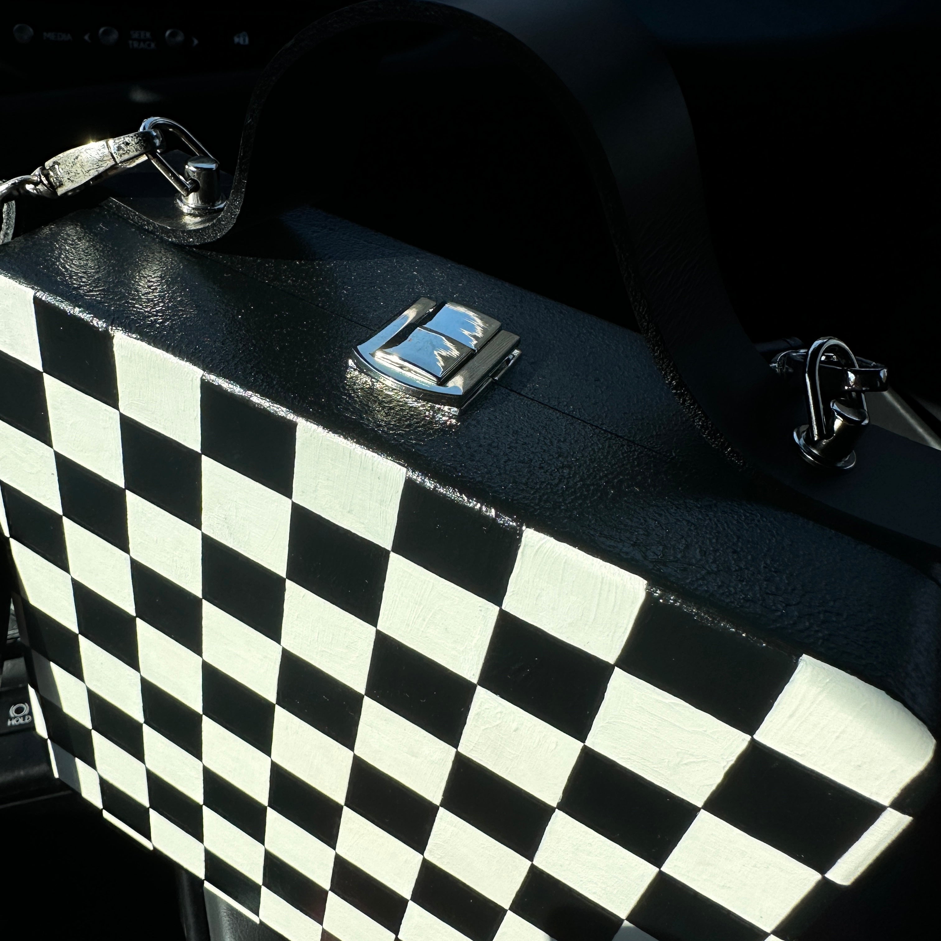 Black and white checkered wooden handbag with leather strap on car seat, handmade artistic accessory.