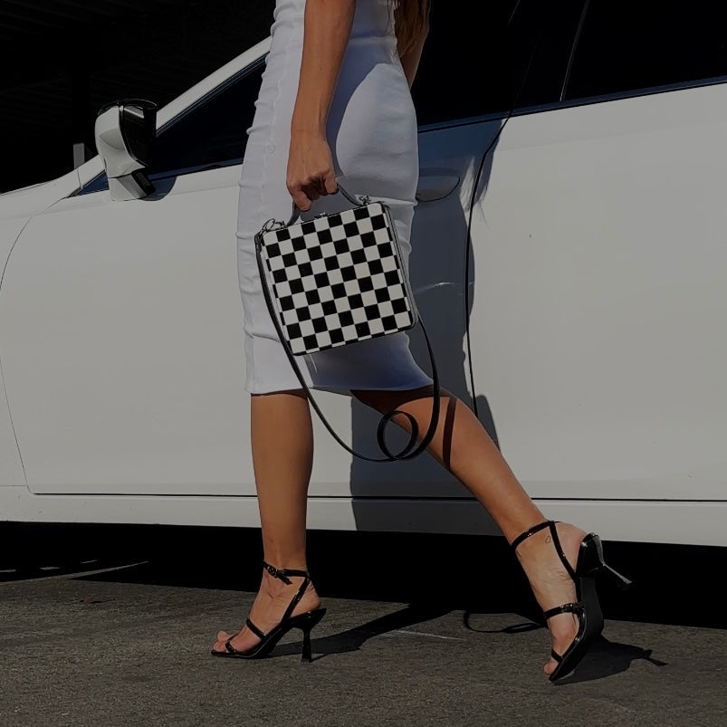 Black and white checkered wooden handbag with leather strap on car seat, handmade artistic accessory.